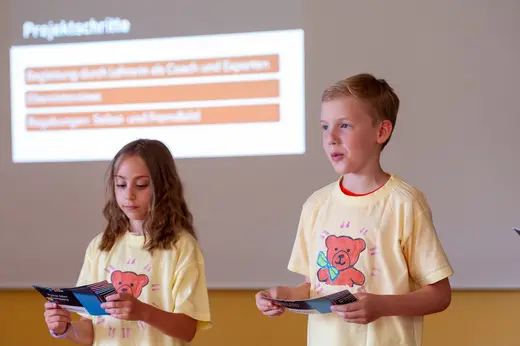 Zwei Kinder präsentieren die Arbeitsschritte ihrer Junior Mini Company